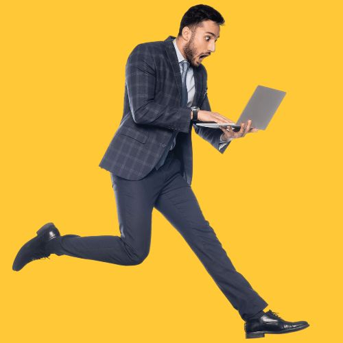 Professional man in a tailored suit leaping mid-air on a bright yellow background, looking surprised at his laptop screen—representing the fast-paced nature of IT Recruitment in Ghana.
